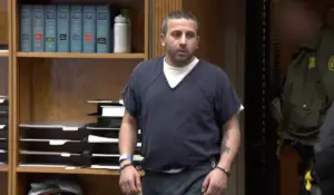 Man in jail clothing and handcuffs stands in a courtroom during a sentencing hearing.